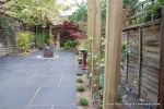 Small town house garden with a Japanese feel black limestone random paving installed with a centre slate water feature, Timber arbour constructed and garden planted with feature plants  