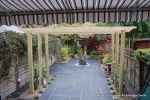 Small town house garden with a Japanese feel black limestone random paving installed with a centre slate water feature, Timber arbour constructed and garden planted with feature plants  