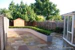 New lawn, planting, shed and fence patio was constructed using fossil sandstone in 4 sizes laid to a random pattern with a curved block planter wall painted in gun ship grey and planted with a topiary hedge.